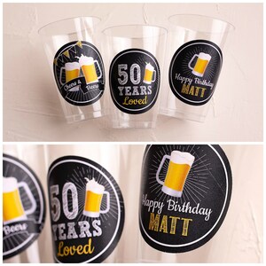 Op de afbeelding: Transparante plastic bekers met zwarte en gouden etiketten. De etiketten tonen biermokken en de teksten "Cheers & Beers", "50 Years Loved" en "Happy Birthday MATT". Geschikt voor een verjaardagsfeest.