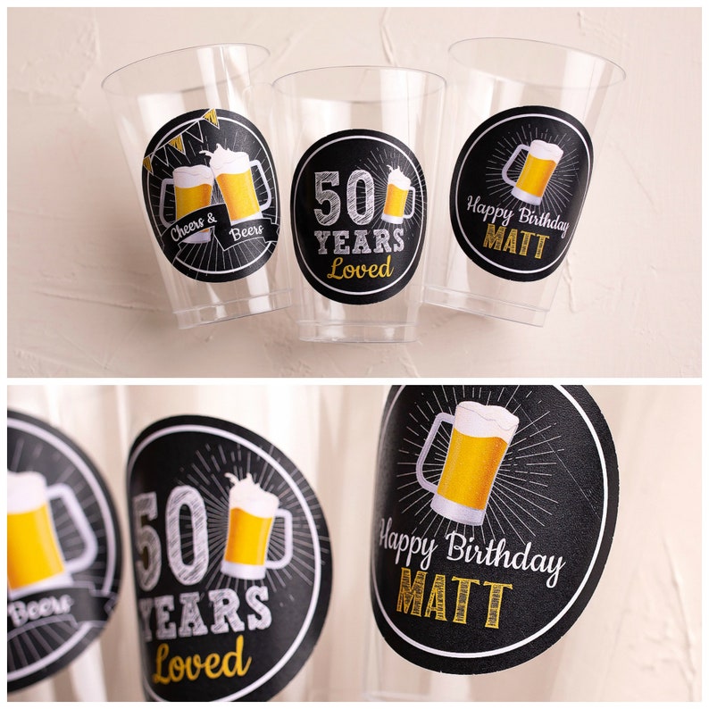 Op de afbeelding: Transparante plastic bekers met zwarte en gouden etiketten. De etiketten tonen biermokken en de teksten "Cheers & Beers", "50 Years Loved" en "Happy Birthday MATT". Geschikt voor een verjaardagsfeest.