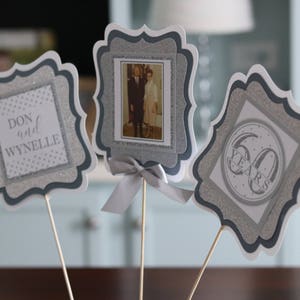 May include: Three silver and white table centrepieces with a decorative border. The centrepieces feature a photo of a couple, the names "Don and Wynnelie", and the text "60 Years".