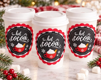 May include: Three white disposable cups with lids, each featuring a black circular label with a red scalloped border. The label displays the text "hot cocoa" in white script, a graphic of a red mug with whipped cream, and white snowflakes.