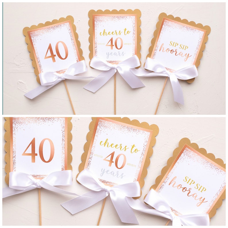 Puede incluir: Cuatro toppers de cupcake dorados y blancos con bordes festoneados. Los toppers presentan el texto "cheers to 40 years" y "sip sip hooray".