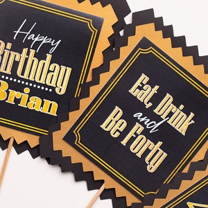 May include: Four black and gold party signs with scalloped edges. The signs have gold lettering on a black background. The text on the signs reads "Happy Birthday Brian", "Eat and Drink", "Be Forty", and "Cheers to 40".