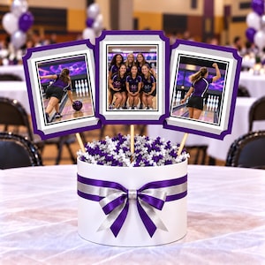 May include: A white cylindrical centerpiece box decorated with a purple and silver ribbon bow, filled with purple and silver paper filler. Three rectangular photo frames on wooden sticks display images of people bowling in purple shirts.