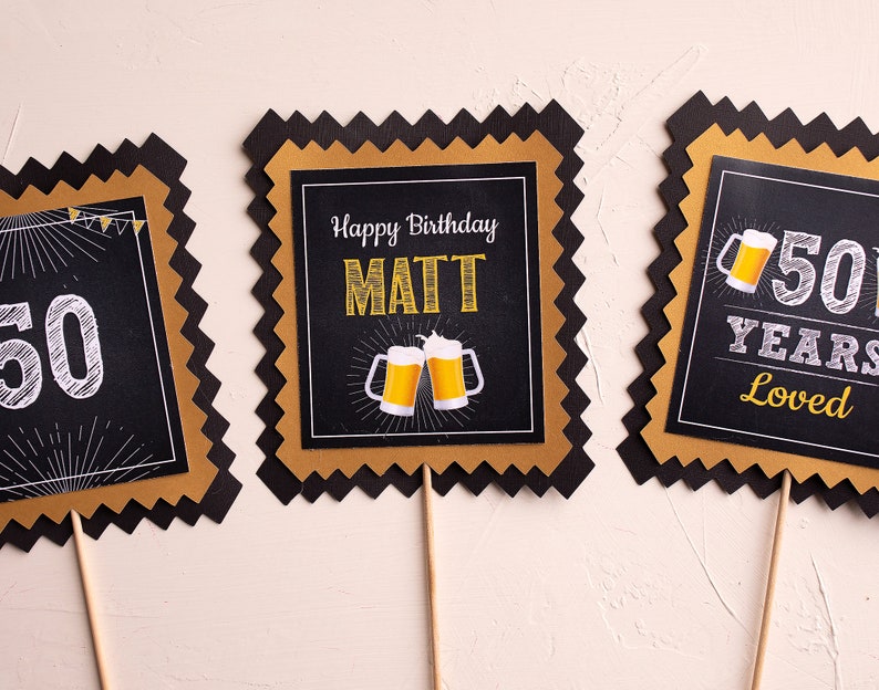 May include: Three black and gold party decorations with a scalloped edge. The centre decoration says "Happy Birthday MATT" with two beer mugs. The left decoration says "50" and the right decoration says "50 YEARS LOVED".