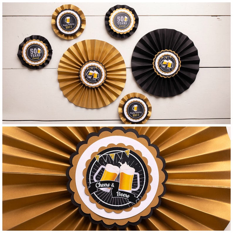 Op de afbeelding: Gouden en zwarte papieren waaierdecoraties met cirkelvormige centerpieces. De centerpieces tonen biermokken en de tekst "Cheers & Beers" en "50 Years Loved". Sommige centerpieces hebben de naam "Matt".