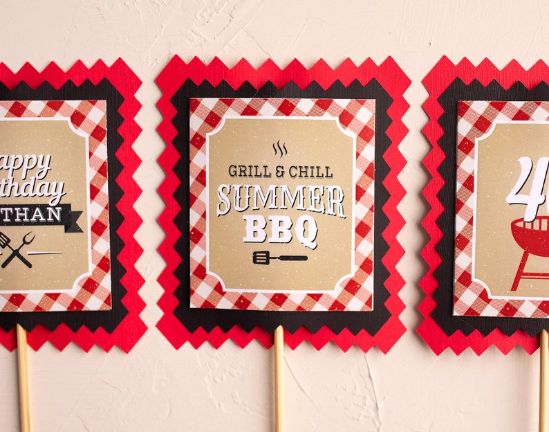 Puede incluir: Tres letreros decorativos sobre palitos de madera. Los letreros tienen un borde a cuadros rojo y blanco, ribete negro y bordes en zigzag rojos. Los letreros tienen el texto "Happy Birthday", "Grill & Chill Summer BBQ" y "40".