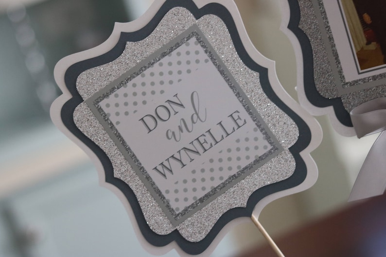 May include: A silver and black glitter card with a white square in the centre. The text "DON and WYNELLE" is printed in black on the white square.