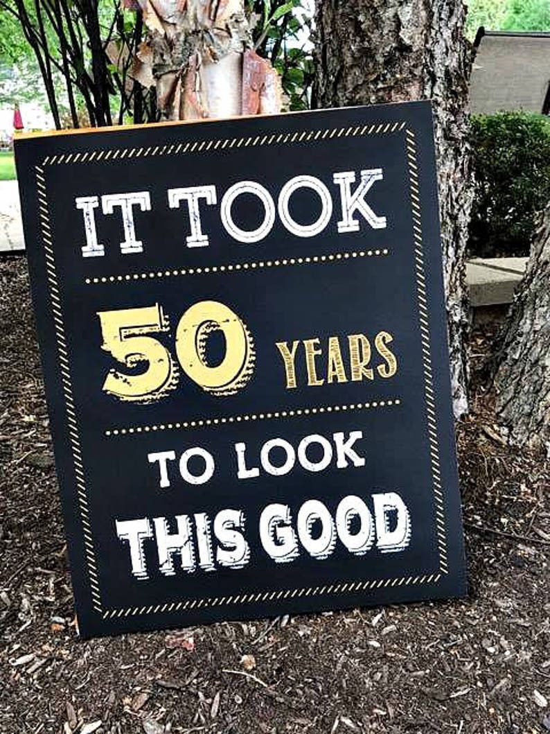 May include: Black chalkboard sign with gold lettering that reads "It took 50 years to look this good".