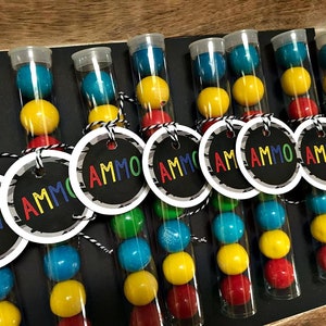 May include: Nine clear plastic tubes filled with colorful candy, each with a black and white circle tag that says "AMMO".