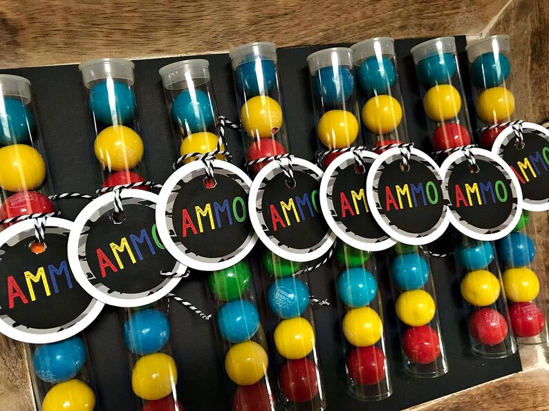May include: Nine clear plastic tubes filled with colorful candy, each with a black and white circle tag that says "AMMO".