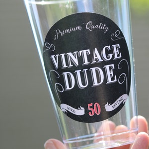 May include: A clear plastic cup with a black and white sticker that says "Premium Quality Vintage Dude Aged 50 Vintage".