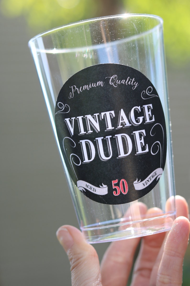 May include: A clear plastic cup with a black and white sticker that says "Premium Quality Vintage Dude Aged 50 Vintage".