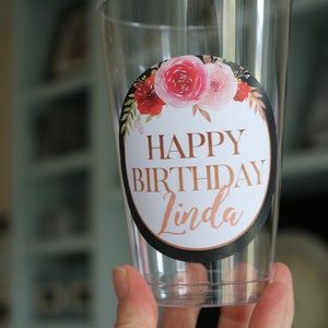 May include: Clear plastic cup with a round sticker that says "Happy Birthday Linda" in gold lettering with a floral design in pink, red, and green.