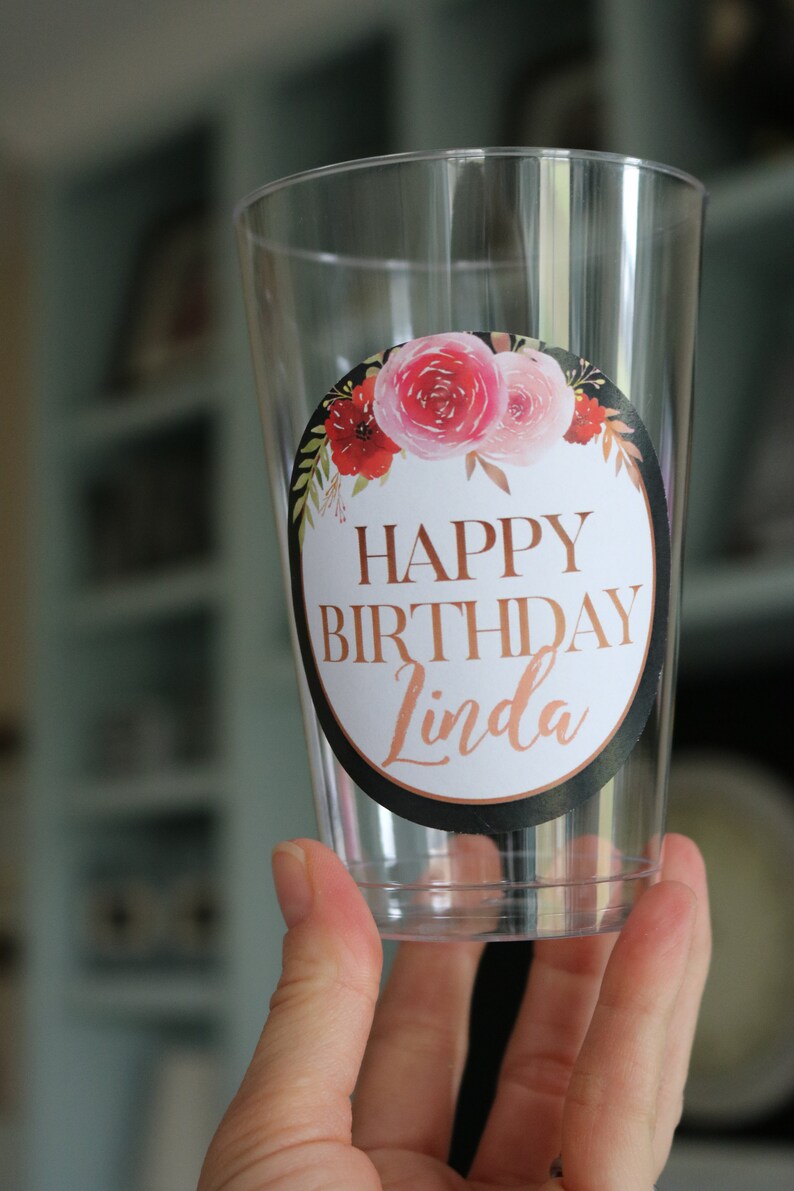 May include: Clear plastic cup with a round sticker that says "Happy Birthday Linda" in gold lettering with a floral design in pink, red, and green.