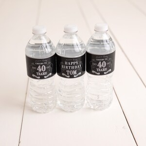 May include: Three clear plastic water bottles with black and silver labels. The labels say "Cheers to 40 Years!" and "Happy Birthday Tom".