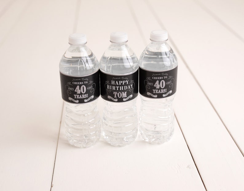 May include: Three clear plastic water bottles with black and silver labels. The labels say "Cheers to 40 Years!" and "Happy Birthday Tom".
