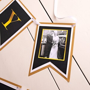Puede incluir: Bandera negra y dorada con una foto de una pareja en blanco y negro. La bandera est&aacute; hecha de cartulina y tiene un borde dorado. La foto es de una pareja en su atuendo de boda, de pie frente a un coche.