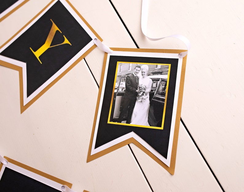 Puede incluir: Bandera negra y dorada con una foto de una pareja en blanco y negro. La bandera est&aacute; hecha de cartulina y tiene un borde dorado. La foto es de una pareja en su atuendo de boda, de pie frente a un coche.