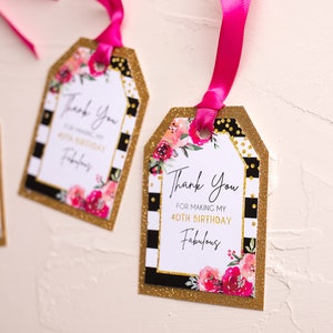 以下が含まれることがあります： ピンクの花柄と白い文字で「私の40歳の誕生日を素晴らしいものにしてくれてありがとう」と書かれた、金色と黒色のギフトタグです。