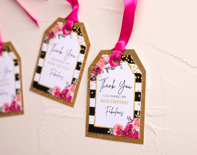 以下が含まれることがあります： ピンクの花柄と白い文字で「私の40歳の誕生日を素晴らしいものにしてくれてありがとう」と書かれた、金色と黒色のギフトタグです。