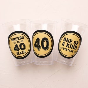 May include: Three clear plastic cups with black and gold stickers. The stickers say "Cheers to 40 Years", "40" and "One of a Kind Vintage".