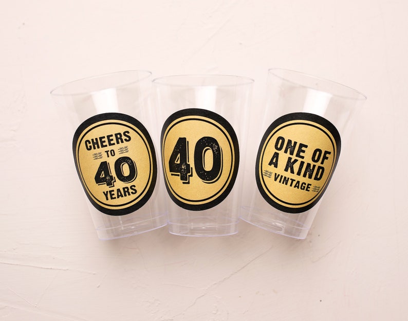 May include: Three clear plastic cups with black and gold stickers. The stickers say "Cheers to 40 Years", "40" and "One of a Kind Vintage".