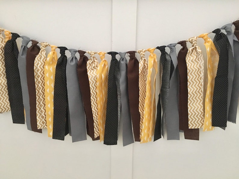 May include: A fabric banner with a mix of yellow, brown, gray, and black fabric strips. The strips are tied together to create a garland.