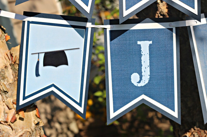 Op de afbeelding: Blauw-witte afstudeerbanner met een afstudeerhoed en de letter "J" erop gedrukt.