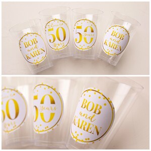 May include: Four clear plastic cups with gold and white round stickers. The stickers have gold text that says "Bob and Karen" and "50 Years".