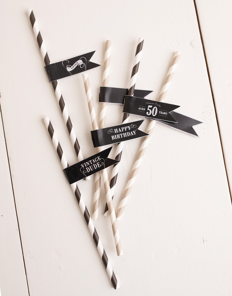 Puede incluir: Pajitas de papel rayadas en blanco y negro con banderas negras. Las banderas tienen el texto "Vintage Dude", "Happy Birthday" y "Aged 50 Years".