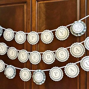 May include: A white and silver banner with the words "Happy 60th Anniversary Paul" in a circle design. The banner is hanging on a wooden door.