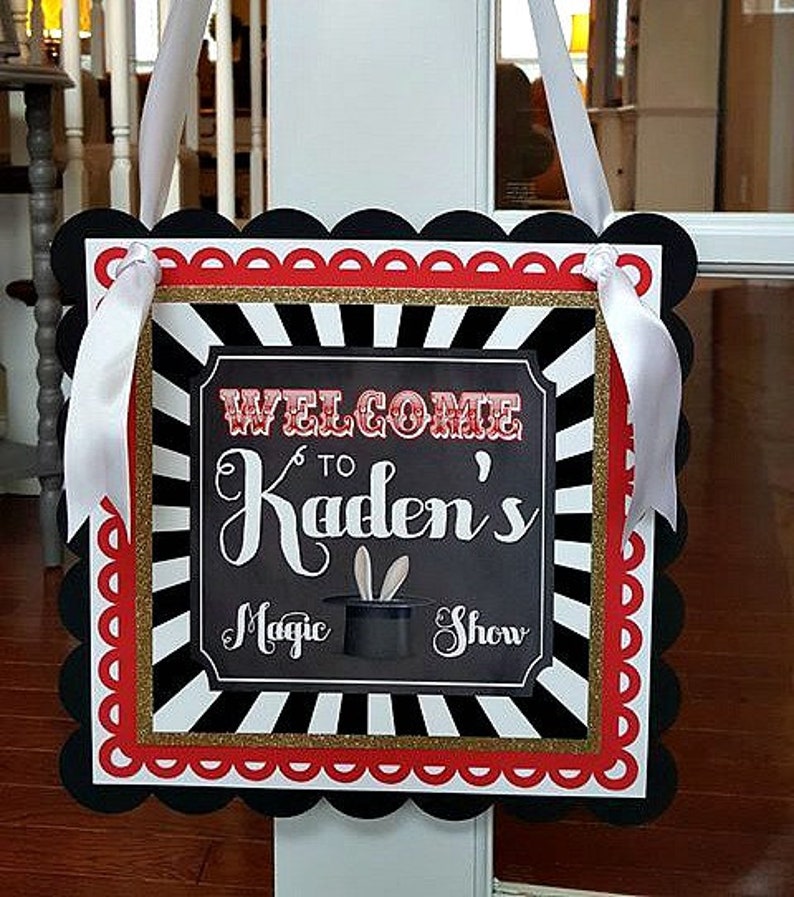 May include: Black and white striped welcome sign with red and gold trim. The sign says "Welcome to Kaden's Magic Show".