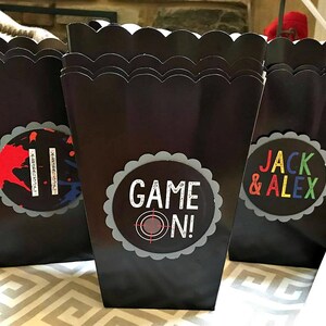 May include: Three black popcorn boxes with scalloped edges. The boxes have colorful labels with the text "Game On!" and "Jack & Alex".