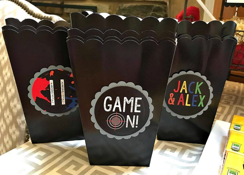 May include: Three black popcorn boxes with scalloped edges. The boxes have colorful labels with the text "Game On!" and "Jack & Alex".