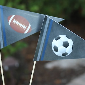 May include: Two gray pennant flags with blue stripes. One flag has a brown football with white laces. The other flag has a black and white soccer ball.