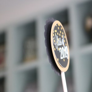 May include: Black and gold graduation party cupcake topper with the text "Class of 2019".