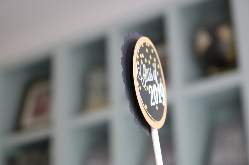 May include: Black and gold graduation party cupcake topper with the text "Class of 2019".