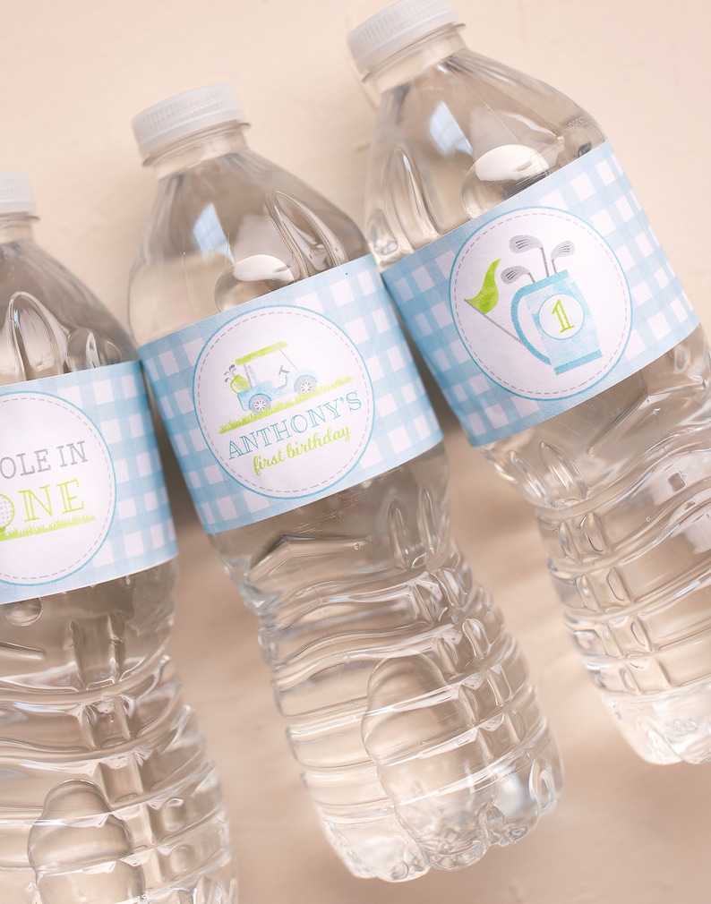 Puede incluir: Tres botellas de agua de pl&aacute;stico transparente con etiquetas de cuadros azules y blancos. Las etiquetas tienen un carrito de golf y palos de golf con el texto "Anthony's first birthday" en una botella y "Hole in One" en otra botella.