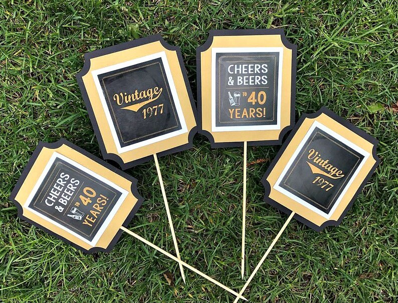 May include: Four black and gold square signs with white text. The signs say "Cheers & Beers to 40 Years!" and "Vintage 1977".