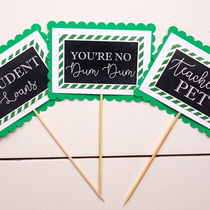May include: Three green and white signs with black chalkboard inserts. The signs have scalloped edges and are on wooden sticks. The signs read "Student Loans", "You're No Dum Dum", and "Teacher's Pet".