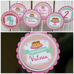 May include: Pink and green cupcake toppers with a pancake and pajamas theme. The toppers feature a pancake stack, a plate with a pancake, a pair of pajamas, and the text "Pancakes and Pajamas" and "Happy Birthday Victoria".