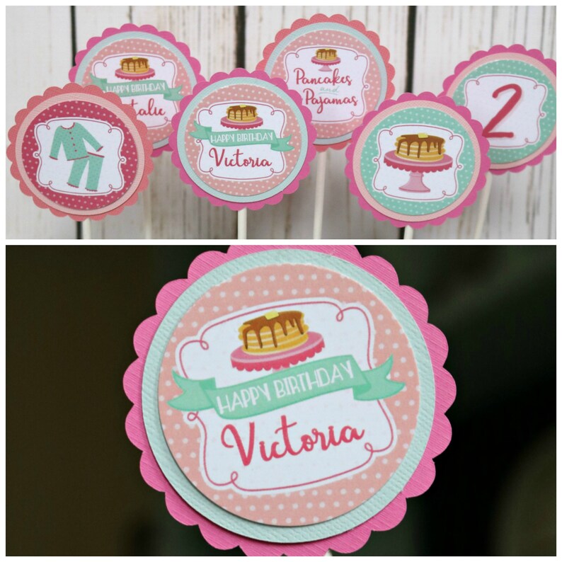 May include: Pink and green cupcake toppers with a pancake and pajamas theme. The toppers feature a pancake stack, a plate with a pancake, a pair of pajamas, and the text "Pancakes and Pajamas" and "Happy Birthday Victoria".