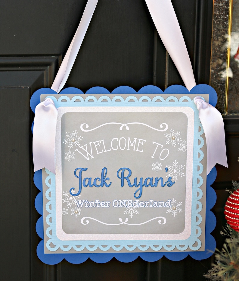 May include: A gray and blue welcome sign with white scalloped edges. The sign says "Welcome to Jack Ryan's Winter Wonderland".