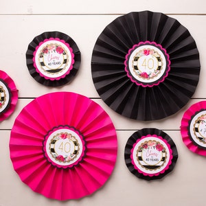 以下が含まれることがあります： 金色のアクセントと花柄のデザインが施された、黒とピンクの紙製扇風機6個。扇風機には、「Cheers to 40 Years」と「40 & Fabulous」の文字が印刷されています。