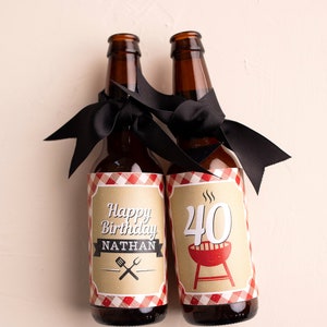 Puede incluir: Dos botellas de cerveza marrones con cintas negras atadas al cuello. Una botella tiene una etiqueta que dice "Happy Birthday Nathan" con utensilios cruzados. La otra botella tiene una etiqueta con el n&uacute;mero "40" y una parrilla roja.