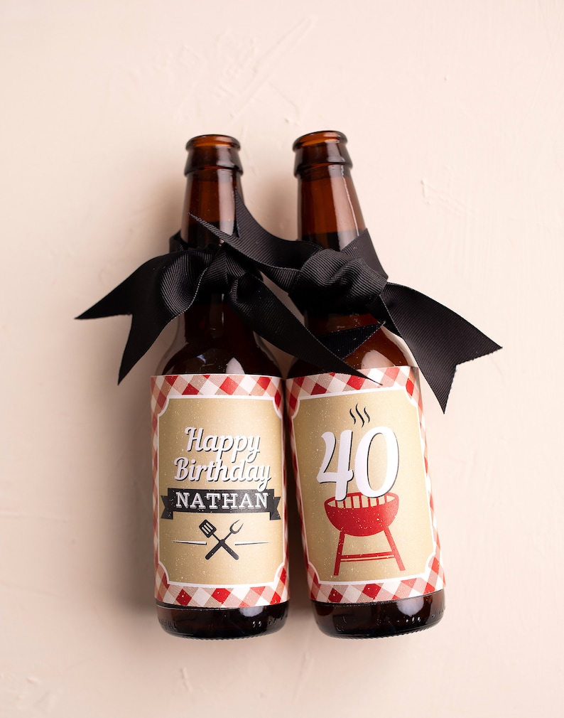 Puede incluir: Dos botellas de cerveza marrones con cintas negras atadas al cuello. Una botella tiene una etiqueta que dice "Happy Birthday Nathan" con utensilios cruzados. La otra botella tiene una etiqueta con el n&uacute;mero "40" y una parrilla roja.