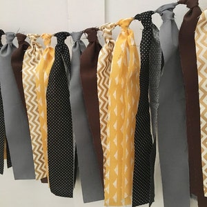 May include: A fabric banner with alternating strips of yellow, brown, black, and gray fabric. The fabric has different patterns, including polka dots, chevron, and geometric designs.