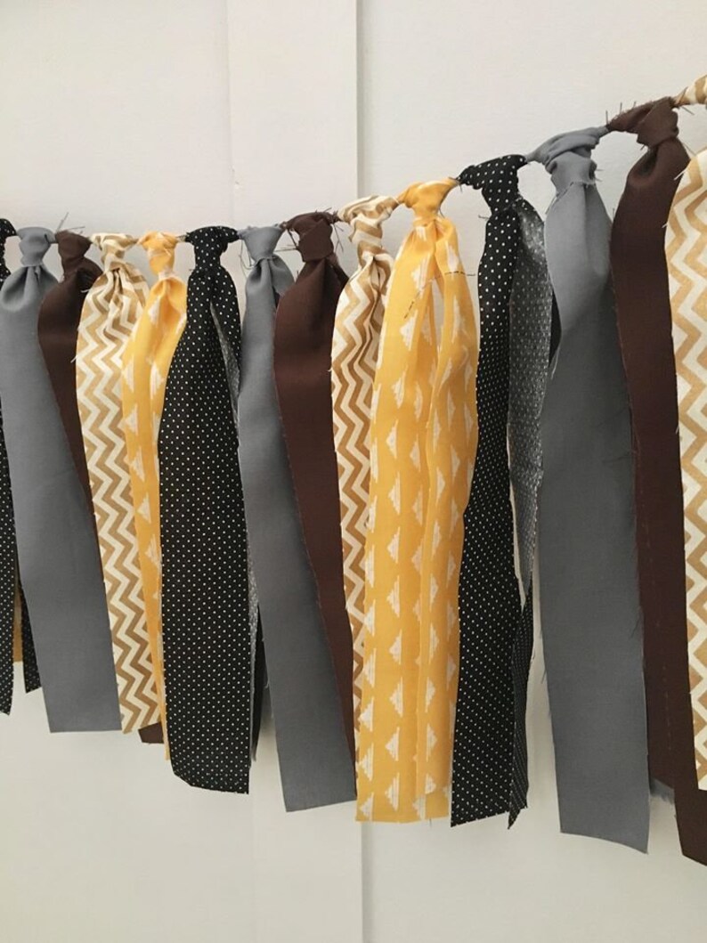 May include: A fabric banner with alternating strips of yellow, brown, black, and gray fabric. The fabric has different patterns, including polka dots, chevron, and geometric designs.