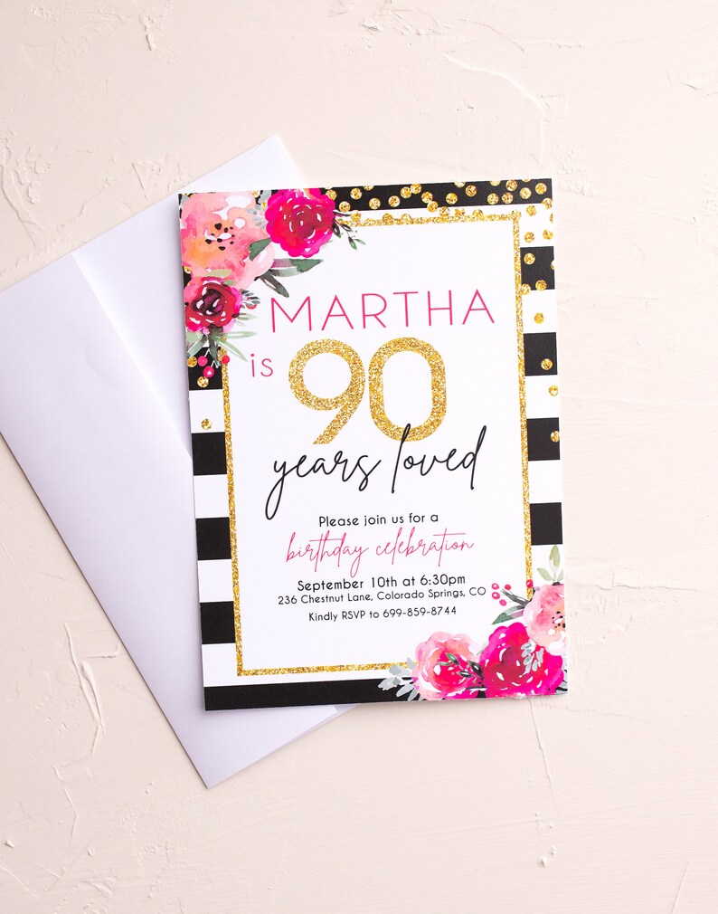 May include: A birthday invitation with a floral design and the text "MARTHA is 90 years loved." The invitation has a gold glitter border and black and white stripes. A white envelope is next to the invitation.