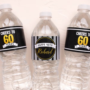May include: Three clear plastic water bottles with custom labels. Two bottles have black labels with "Cheers to 60 Years" in white and gold. The centre bottle has a label that says "Happy 40th Richard".